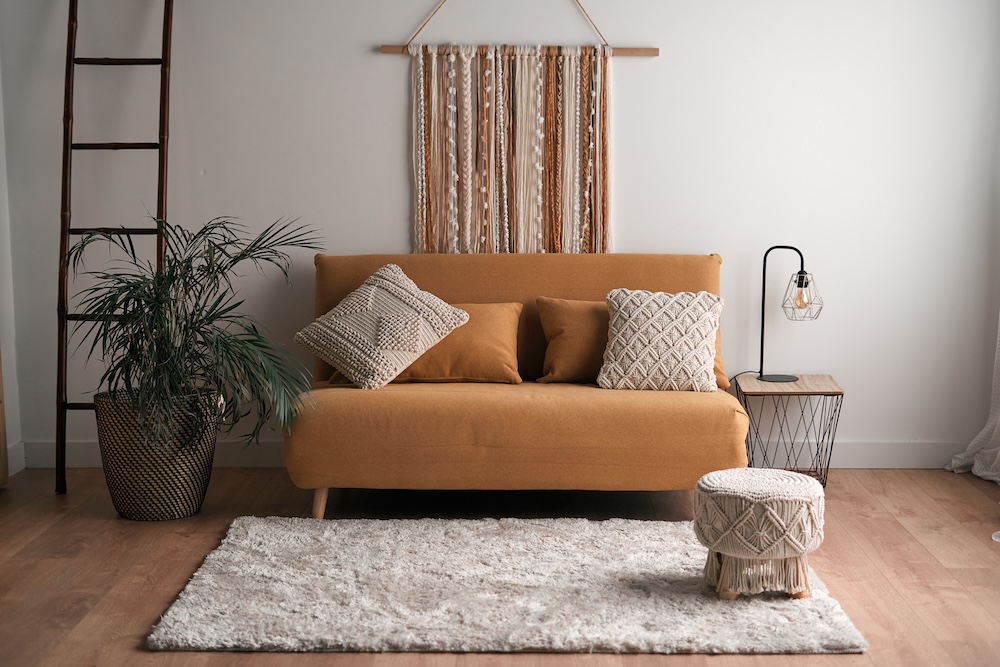 ciekawe pomyły na ścianę w salonie - makrama w stylu boho za rudą kanapą ciekawe pomysły na ścianę w salonie - brązowo-beżowa makrama za sofą
