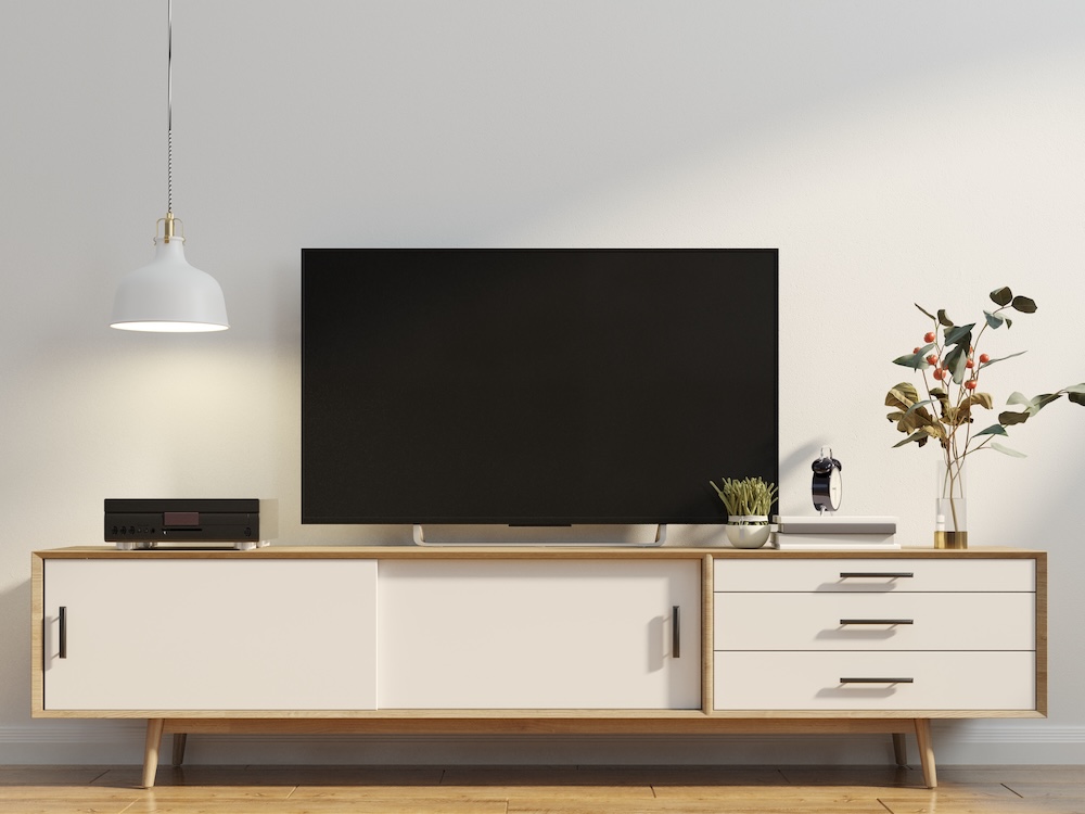 ściana z tv w salonie na niskiej szafki z drewna z jasnymi frontami 