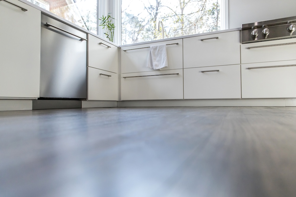spacious large modern white kitchen recently updated with high-end appliances, wood floors, picture windows, white cabinets and wood beams with lots of copy space for text. A woman in workout exercise gear standing in the kitchen. A large amount of hardwo pcv podłoga kuchenna